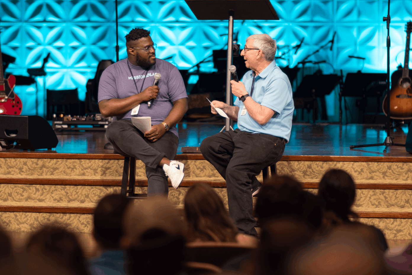 Two men sitting on stools on stage, speaking at Collegiate Summit 2024